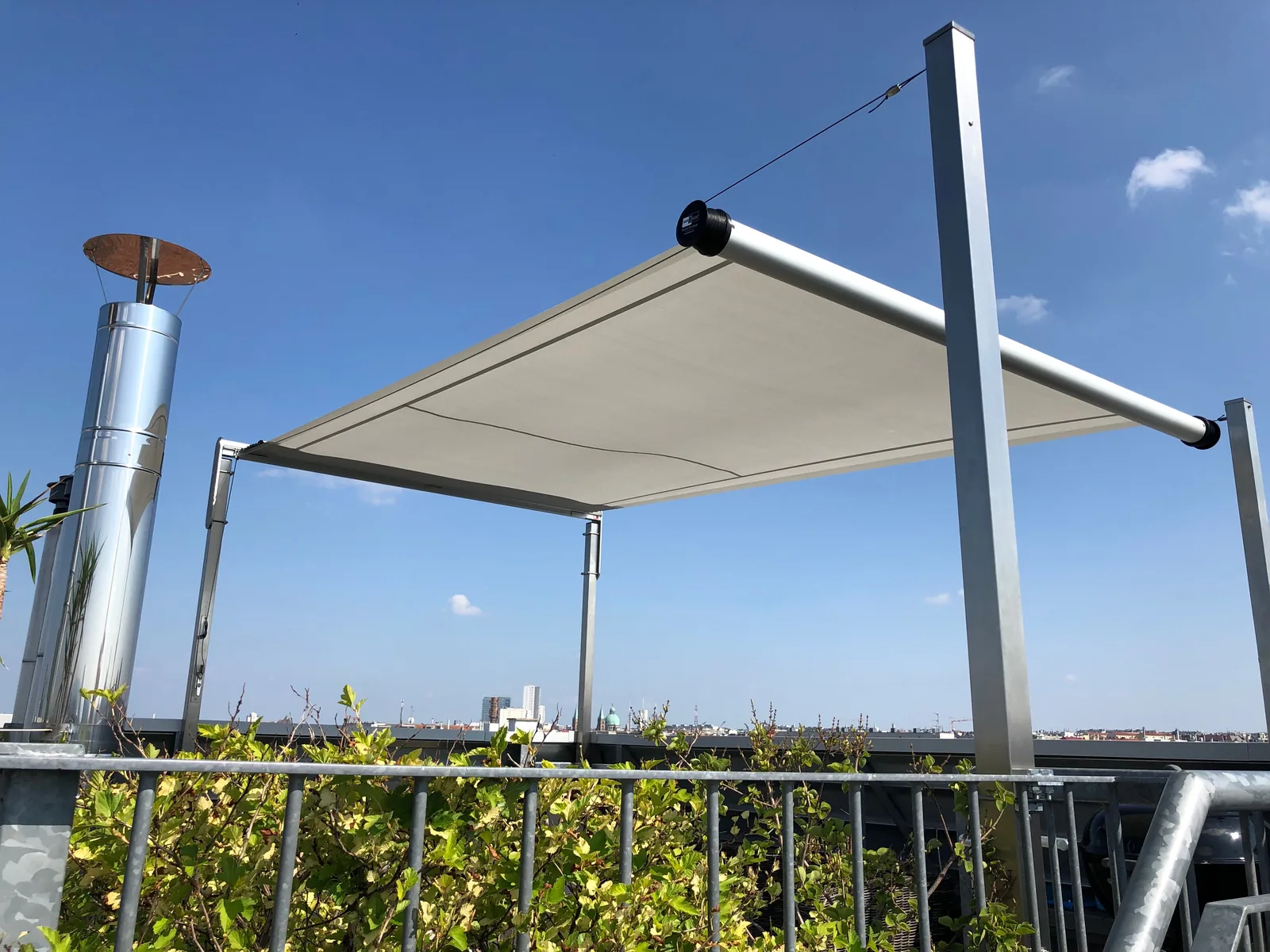 SHADE FRAME auf einer Dachterrasse: freistehendes Sonnensegel an vier Edelstahlpfosten über der Stadt