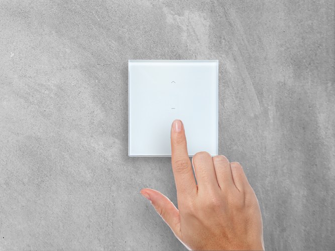 Wandsender Plano 1 von Kaiser Nienhaus an einer Betonwand, ein Finger tippt auf das Glas