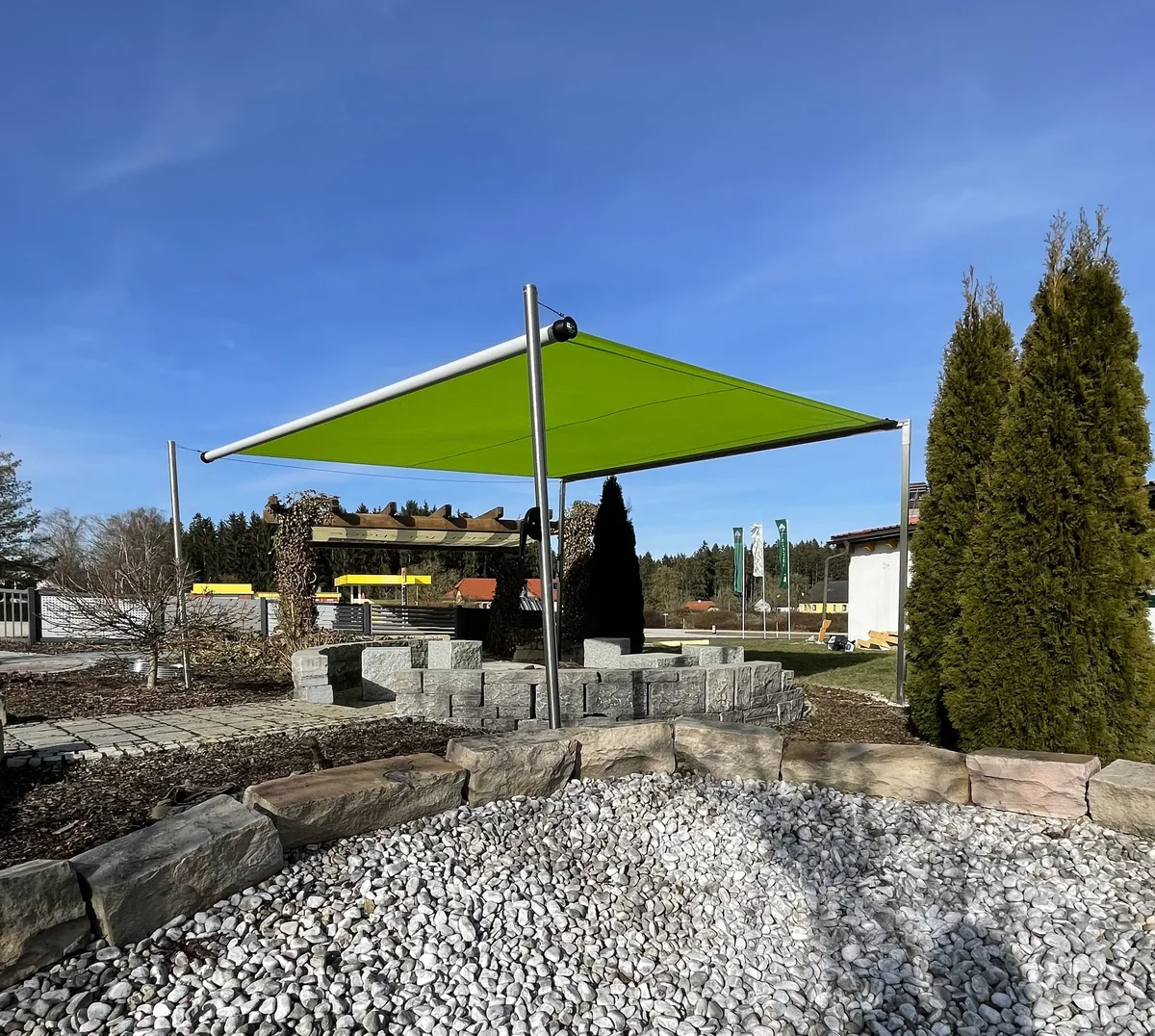 SHADE FRAME mit grüner Segelmembrane im Kiesgarten, leicht geneigt zwischen Edelstahlpfosten