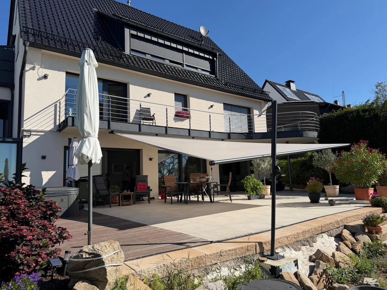 SHADE INOX in der Frontalansicht: rollbares Sonnensegel beschattet Terrasse und Sitzbereich vor der Hausfassade